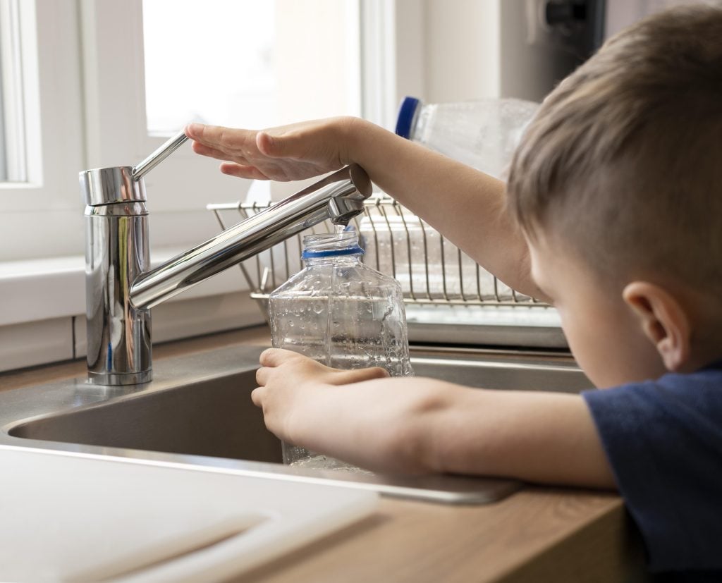 close up kid filling bottle with water