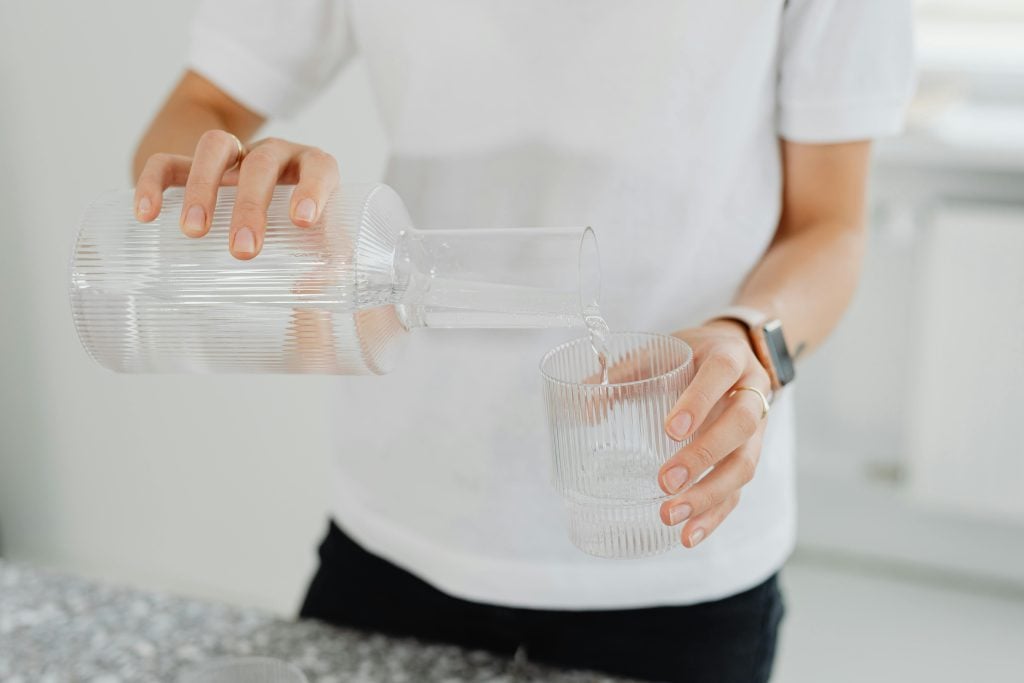 woman wearing a white t-shirt pouring clean water from a jug into a glass